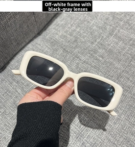 Detail view of beige rectangular sunglasses with black grey lenses held in hand