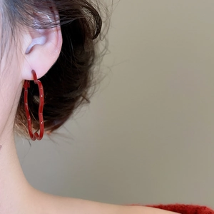 Detail shot of a red heart-shaped hoop earring with wavy texture on female model