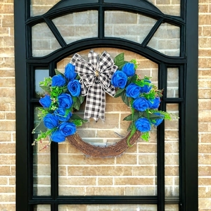 Detail of Christmas wreath with blue roses, checkered bow, and natural vine base