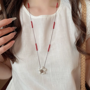 Detail of floral pendant necklace with white pearls and red beads on a black cord strap