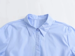 Detail of light blue poplin shirt neckline and shoulder seams on white background