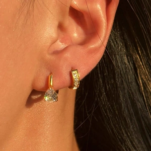 Macro shot of gold teardrop zircon earrings and pavé hoop on a female model ear