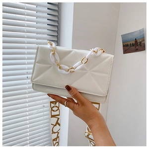 Close-up of white quilted crossbody bag with gold chain and lettered fabric strap