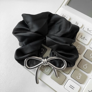 Detail shot of a black satin hair tie with a shiny silver metal bow knot on a white surface