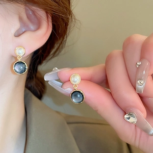 Oval gold plated earrings with white pearl and blue shell inlay shown on model