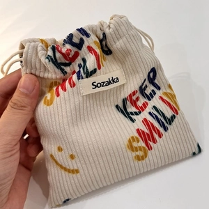 Mano che tiene borsa beige in velluto a coste con stampa Keep Smiling e logo