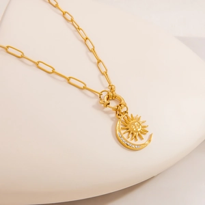 Detailed shot of celestial sun and moon pendant on golden paperclip chain necklace