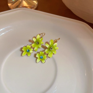 Detailed close-up of green flower drop earrings with rhinestones on a ceramic plate