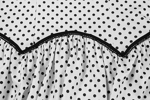 Macro detail of white polka dot dress featuring black wavy lace trim and gathered fabric