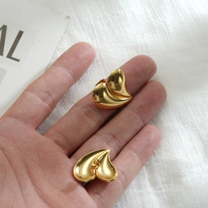 Handheld display of trendy golden heart-shaped stainless steel earrings on white background