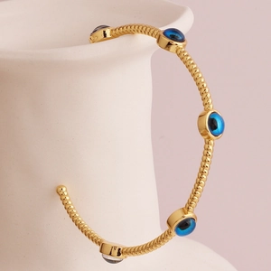Close-up of gold-plated twisted bangle featuring five blue evil eye charms on a vase