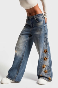 Detail view of high waist blue jeans with yellow floral embroidery and cut-out side design