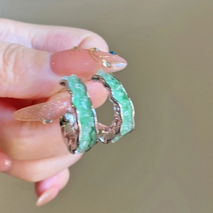 Détail de boucles d'oreilles en C argentées avec pierres vertes tenues à la main