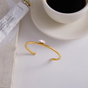 Detail of gold-plated bangle featuring a marquise-cut zircon gemstone on a white desk