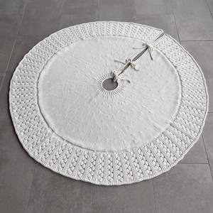 Detail of white knitted Christmas tree skirt with textured pom-pom edge and tie closures