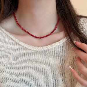 Detail of red glass beaded necklace worn over a white sweater for minimalist style