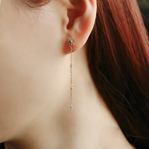 Detail of rose gold long tassel earrings featuring a flower stud and green zircon stones