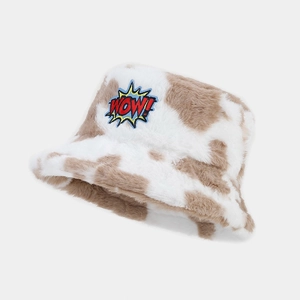Plush cow print bucket hat with 'WOW!' embroidery on a minimalist gray background