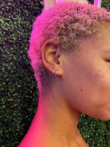 Side view of small S925 sterling silver hoop earrings worn on an earlobe with purple lighting