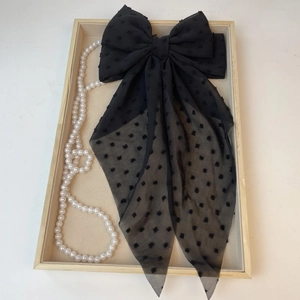 Detail of French style black polka dot chiffon bow hair clip on a wooden tray with pearls
