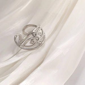 Detailed shot of a silver hollow flower ring with diamonds on white silk fabric