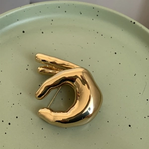 Gros plan d'une broche main OK dorée avec une finition métallique artistique polie