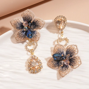 Détail de boucles d'oreilles fleurs asymétriques avec strass et broderie