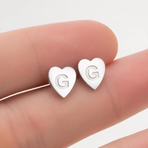 Macro de boucles d'oreilles cœur en argent avec gravure G tenue par la main