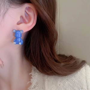 Close-up of blue bear-shaped earrings with white rhinestones on model ear