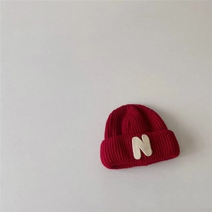 Close-up of red ribbed knit beanie featuring a white letter N patch and folded cuff