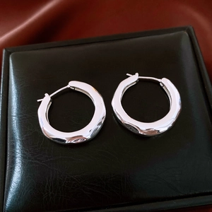 Macro shot of polished silver pleated hoop earrings on black leather and red satin fabric