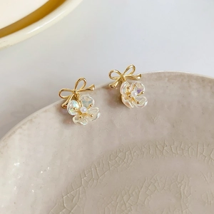 Detail of gold bow earrings featuring iridescent flowers and central pearl accents