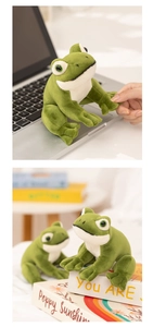 Close-up of cute green plush frog sitting on a desk next to books and a laptop