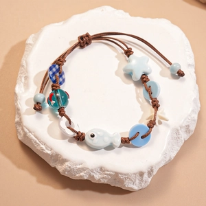 Detail of a handmade ocean-style braided bracelet with blue fish and star beads on stone