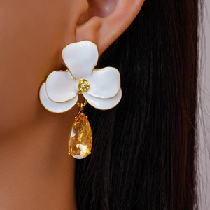 Gros plan de boucles d'oreilles fleurs en émail blanc avec gouttes en cristal jaune