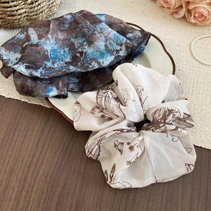 Detail of floral chiffon scrunchies in cream and navy blue displayed on a porcelain plate