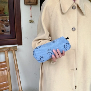 Detail of light blue corduroy cosmetic bag with black smiley face print held by hand