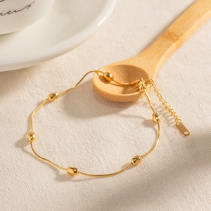 Gold bohemian anklet with small oval beads and lobster clasp on a beige textured background