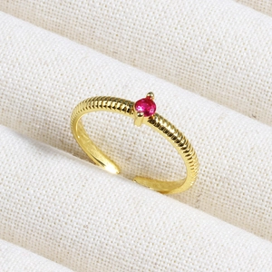 Close-up of golden open ring featuring horizontal texture and a red ruby-colored gemstone