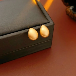 Macro shot of matte golden teardrop earrings on a jewelry box edge with soft lighting
