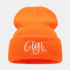 Detailed close-up of Gigi cursive embroidery on orange knitted beanie texture