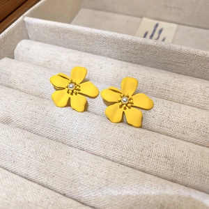 Macro view of yellow floral stud earrings with pearl center in a cream velvet jewelry box