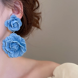 Detail of oversized blue denim rose pendant earrings showing fringe texture on a model