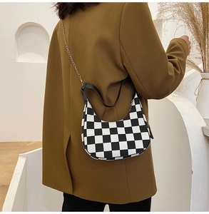 Model wearing a black and white checkered crescent hobo bag with a stylish chain strap