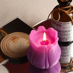 Dettaglio di una candela profumata a forma di tulipano rosa accesa su disco di legno