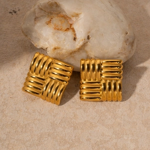 Detailed macro shot of square 18k gold earrings with textured woven pattern on a stone base