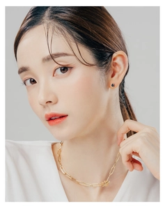 Detail of minimalist gold link chain necklace and black teardrop stud earrings on model