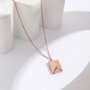 Close-up of rose gold envelope locket pendant on a minimalist white display
