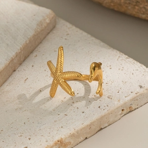 Détail d'une bague ouverte dorée étoile de mer et dauphin sur pierre beige naturelle