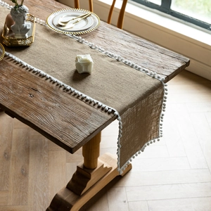 Detail of jute table runner with white pom pom lace trim on a natural wooden table